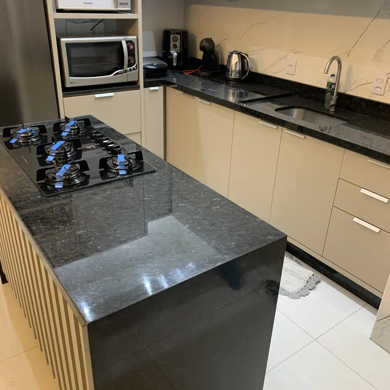 Ilha com cooktop em pedra escura e lateral em cascata